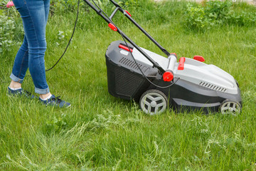 Woman is operating with lawn mower in the garden