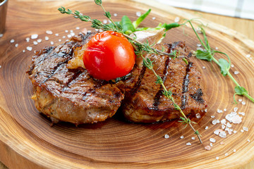 Close up view on tasty grilled steak on wooden board. Composition with cooked beef, herbs and vegetables. Food photo background. Selective focus