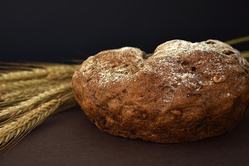 Loaf of bread and ears of wheat on a dark background. Closeup