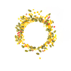 Round frame, border made of green pumpkin seeds, yellow peas and red leaves isolated on white background.