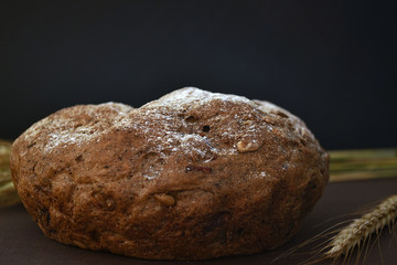 Loaf of bread and ears of wheat on a dark background. Closeup
