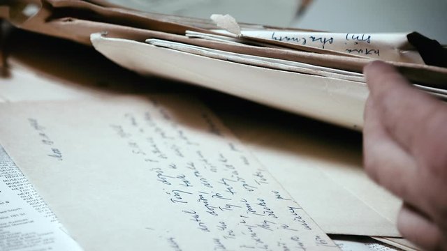 Man searches through pile of old documents and letters. Close up.