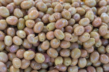 Green olives stacked on a surface as background.