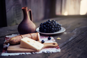 Wine in a clay jug, meat, cheese and grapes lie on a wooden table.