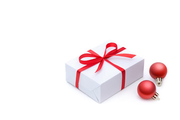 Side view of a white gift box tied with a red satin bright ribbon with a bow and two red festive Christmas balls with empty place for text isolated on white background