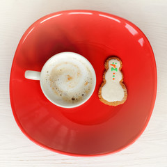 snowman cookie in a plate with a mug of foamy cappuccino top view. Christmas morning coffee
