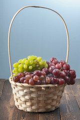 different varieties of ripe grapes in a wicker basket on a dark wooden background