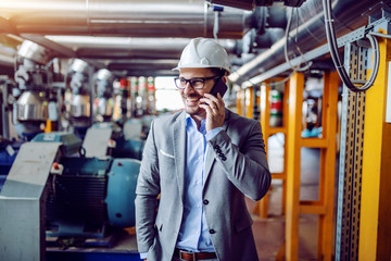 Attractive smiling caucasian businessman in suit and with helmet on head talking on the phone while...