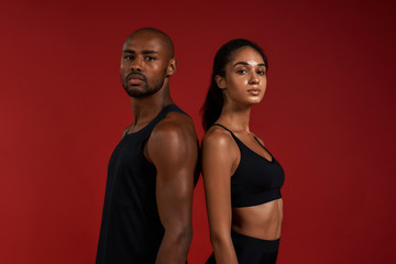 Working out together. Young and confident african fitness couple in sportswear looking at camera while standing against red background