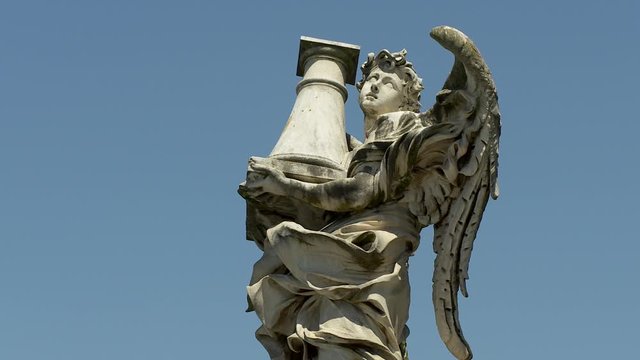 Close-up low angle upper view still shot of a white marble statue by Gian Lorenzo, of an angle with wings carrying a heavy load on his hands against clear blue sky, Rome, Italy