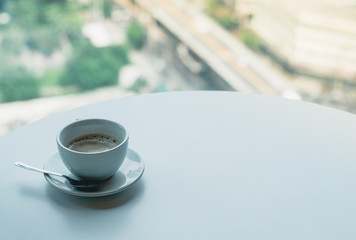 Coffee​ or tea​ cup​ blue color​ on the white​ table through the glass window of a tall building​ background, Business person's break time, Perspective of office lifestyle in big city.
