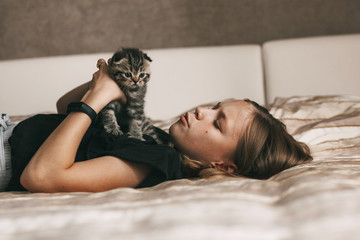 Naklejka premium The child lies on the bed and plays with a British little kitten