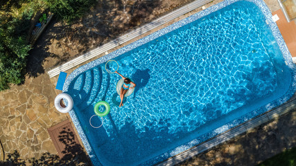 Fototapeta na wymiar Aerial view of beautiful girl in swimming pool from above, swim on inflatable ring donut and has fun in water on family vacation on tropical holiday resort