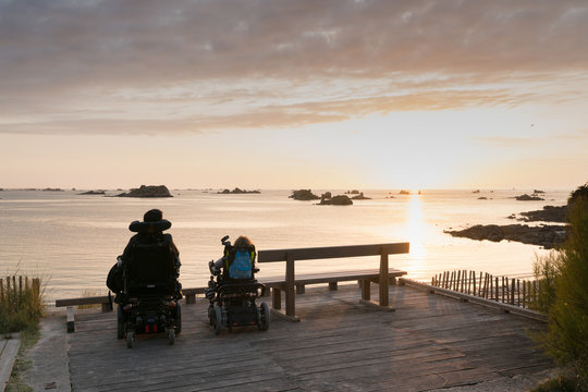 handicapped couple in wheelchairs enjoy a beautiful ocean sunset together from a handicapped beach access viewpoint