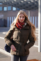 street style fashion portrait of young woman waiting at bus station on a sunny day in winter