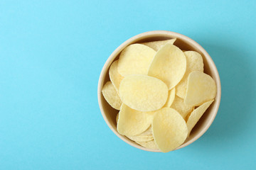 Potato chips in a plate on a colored background top view.