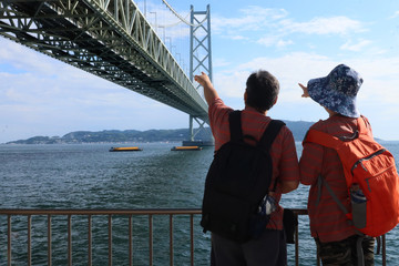 Old couple backpacker stand pointing to the Akachi Kaikyo bridge