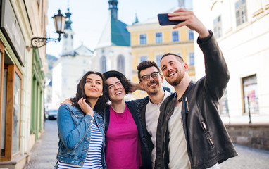 A group of young friends standing outdoor in town, taking selfie.