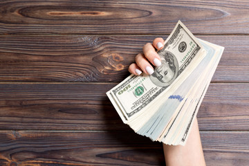Thick bundle of different dollar banknotes in female hand on wooden background. Financial and...