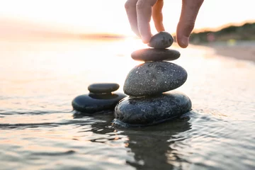 Deurstickers Stenen in het zand Vrouw stapelen donkere stenen op zand in de buurt van zee, ruimte voor tekst. Zen-concept