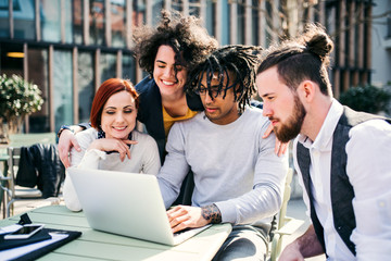 Group of young businesspeople using laptop in courtyard, start-up concept.