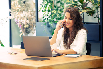 Entrepreneur sales woman having a fun phone chat with a client in a hipster office.