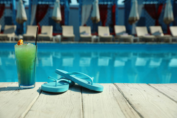 Refreshing cocktail and flip flops near swimming pool on sunny day. Space for text