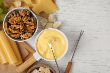 Flat lay composition with pot of tasty cheese fondue and products on white wooden table