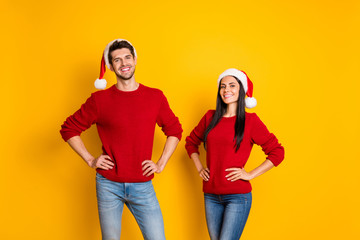 Fototapeta premium Portrait of cheerful spouses in santa claus hats look stand isolated over yellow background