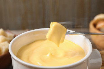 Dipping bread into pot with cheese fondue on table, closeup