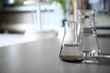Glassware with soil extract and water on grey table, space for text. Laboratory research