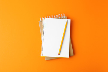 Notebooks with pencil on orange background, top view