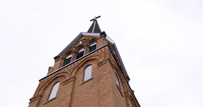 Beautiful tall brick church with cross on top and overcast clouds in the sky