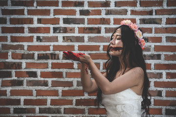 A female ghost or a zombie wearing a white dress with a bloody hand and holding a bloody knife on a brick wall background. Halloween and horror concepts.