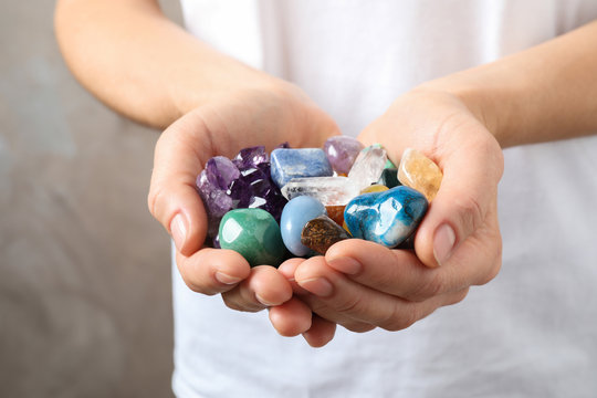 Young Woman Holding Many Beautiful Gemstones On Beige Background, Closeup