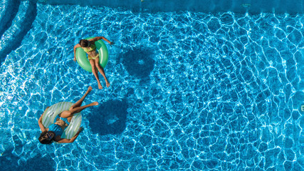 Active children in swimming pool aerial top view from above, happy kids swim on inflatable ring donuts and have fun in water on family holiday vacation on resort