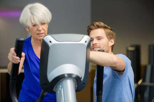 gym worker showing senior woman how to use exercise machine