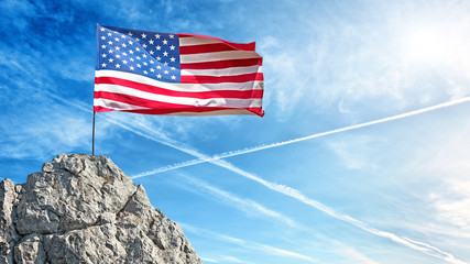 usa flag of united states of america on top of rock against blue clouds sky background side wide view of us national independence symbol flying on flagpole country government sign panorama photo