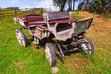 Fototapeta na wymiar An old carriage made of wood with large wheels without a horse on a mountainside on green grass. Retro and vintage from the story.