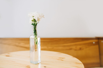 White field flowers in modern transparent vase on a light white background. Cafe interior with wooden table.