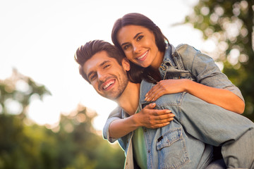 Fototapeta premium Close up photo of pretty girl and guy cuddling piggyback wearing denim jeans outdoors