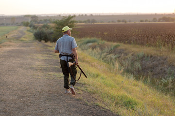 Hunting period, autumn season open. A hunter with a gun in his hands in hunting clothes in the autumn forest in search of a trophy. A man stands with weapons and hunting dogs tracking down the game.	