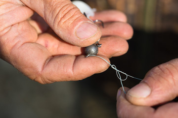 Angler tying a fishing hook to rubber worm lure. Fishing for larva spinning on a lake.