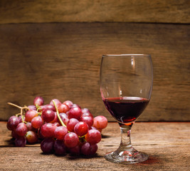 glass of red wine and grapes on wooden table