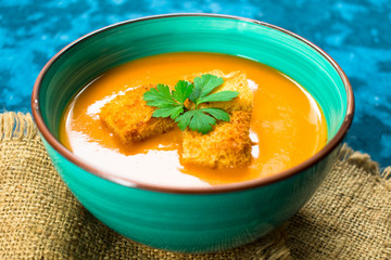 Soup of pumpkin puree and small croutons on a blue background. Close-up. Concept of the autumn menu.