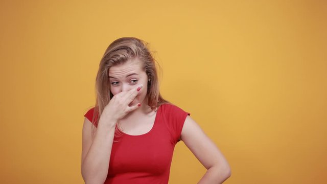 young blonde girl in red t-shirt over isolated orange background shows emotions