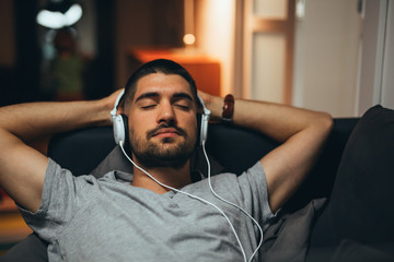 man relaxed on sofa listening music on headphones at his home