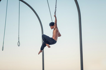 A young man athlete working out on traveling rings on muscle beach, Santa Monica, California