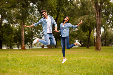 Full length photo of cute pair holding hands jumping high in green park wear denim outfit