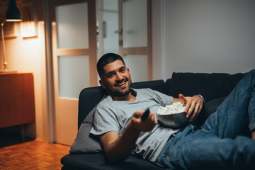 man relaxing on sofa eating popcorn and watching television. evening scene